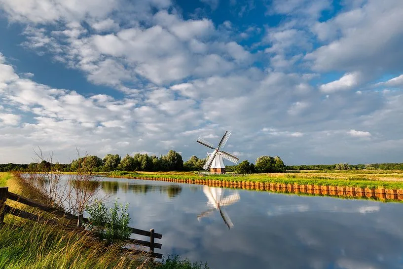 Een witte molen in het open landschap, weerspiegeld in het water